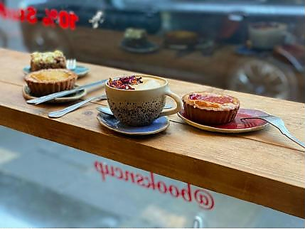 A floral-topped drink and colourful tarts by the café window