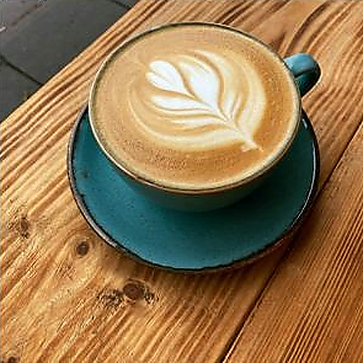 Leaf-shaped latte art in a teal ceramic cup on a wooden table