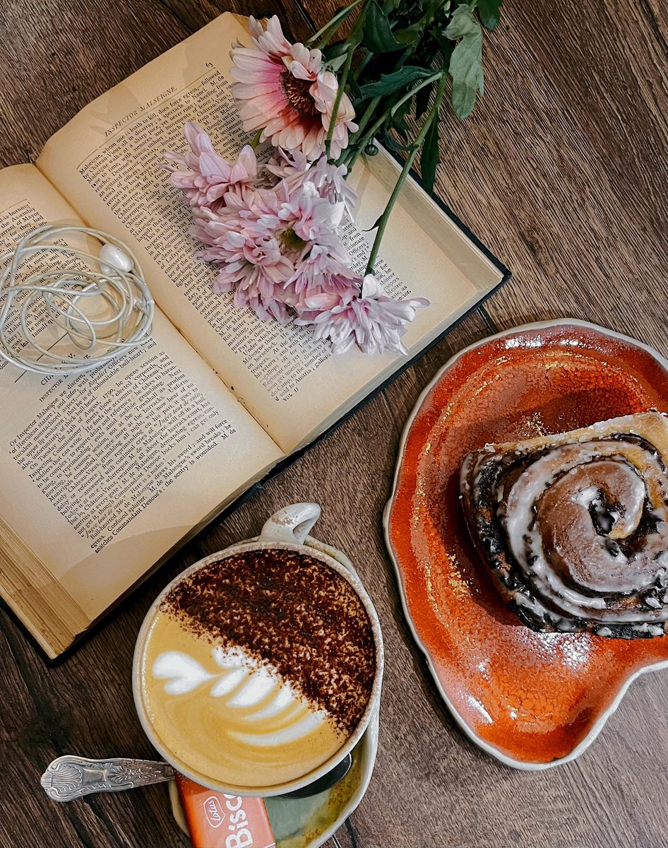 An open book, flowers, a latte and a cinnamon roll