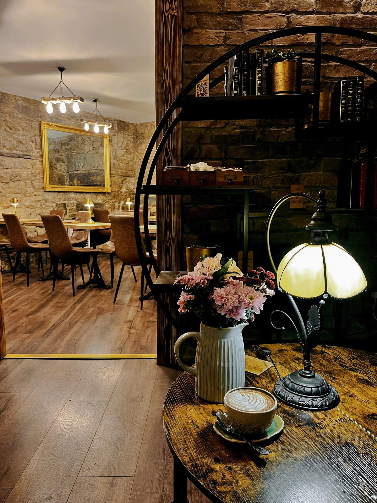 Inside the café — stone walls, the round bookshelf and a flat white by the lamp